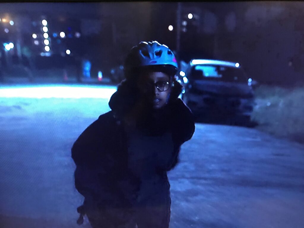 A figure in a bike helmet stands on a dark street at night, in a scene from High Maintenance photographed off a TV screen