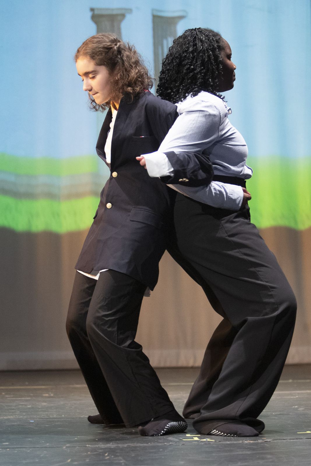 Two teen performers in dark suits lean on each other in a scene in Empowerland, Spring 2026