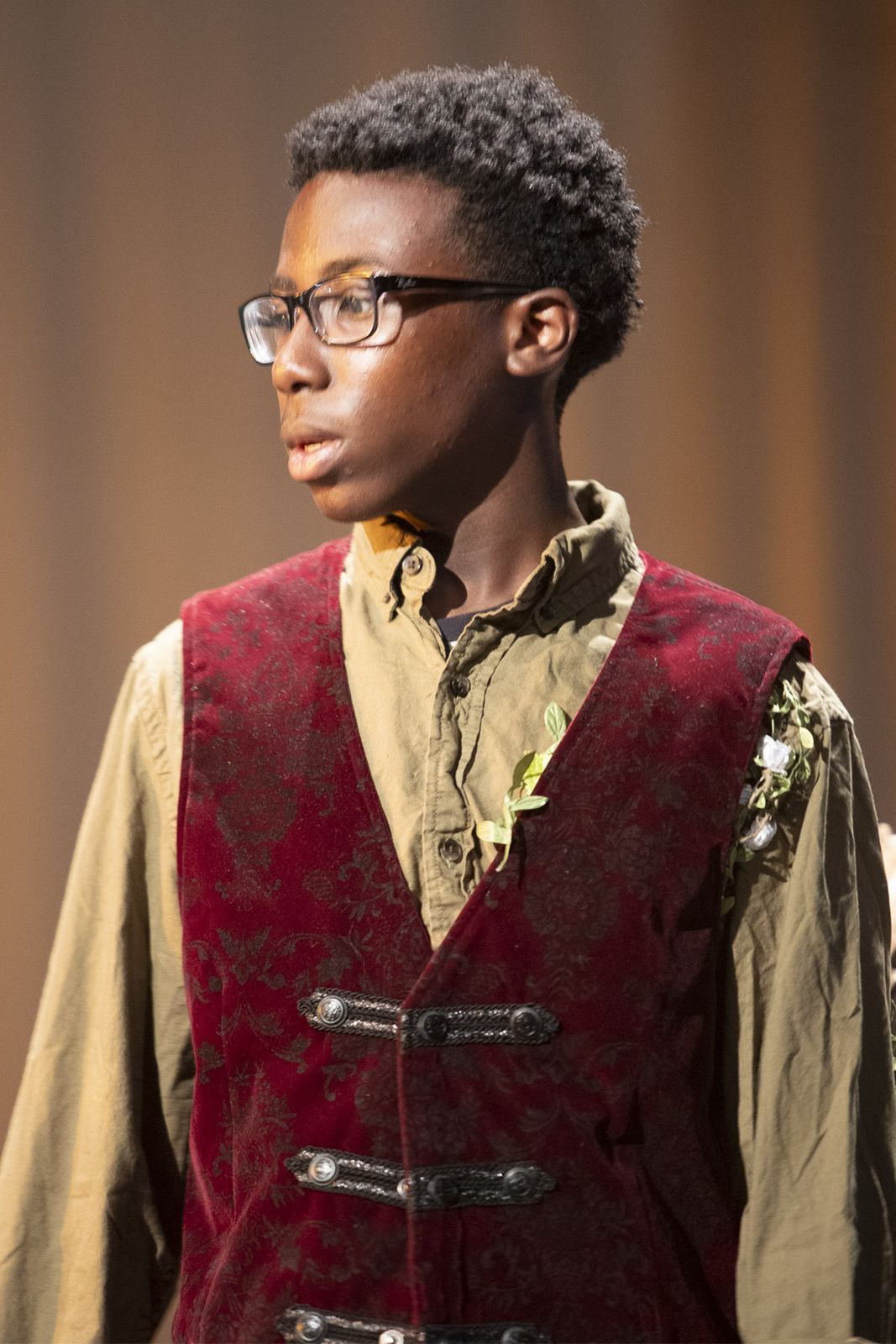 A student in a red velvet vest looks across the stage in The Legend of Tart, Spring 2026