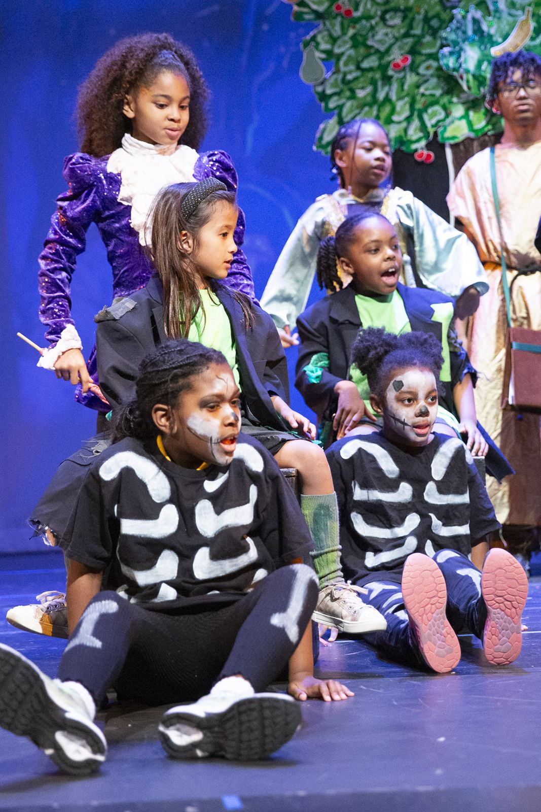 An ensemble in skeleton and storybook costumes sits together on stage in The Mythic Monster Cave, Spring 2026