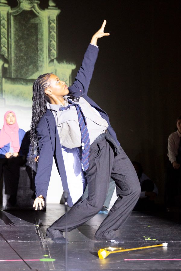 A student in a blazer reaches one arm toward the stage lights