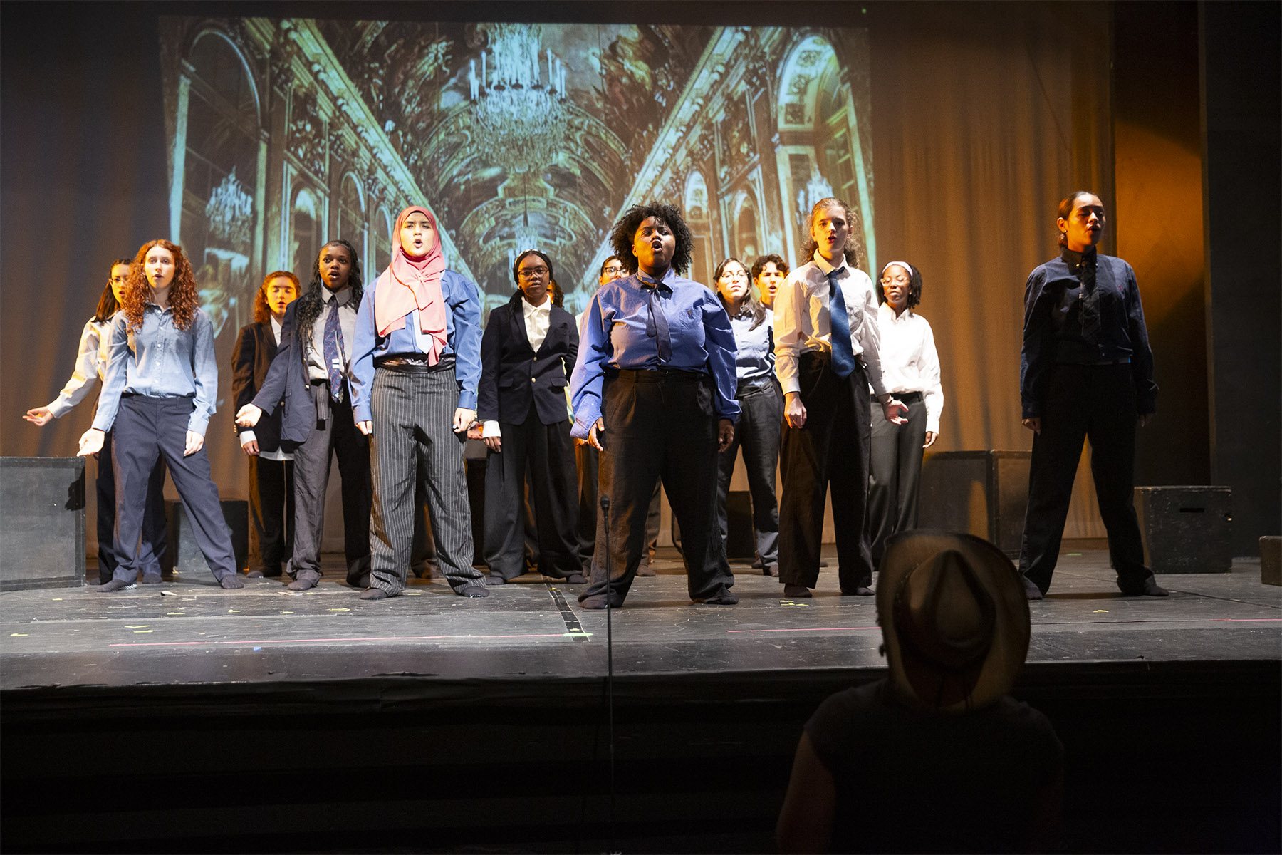 Teen performers in blue and white shirts and dark pants stand in two rows on stage in Empowerland, Spring 2026